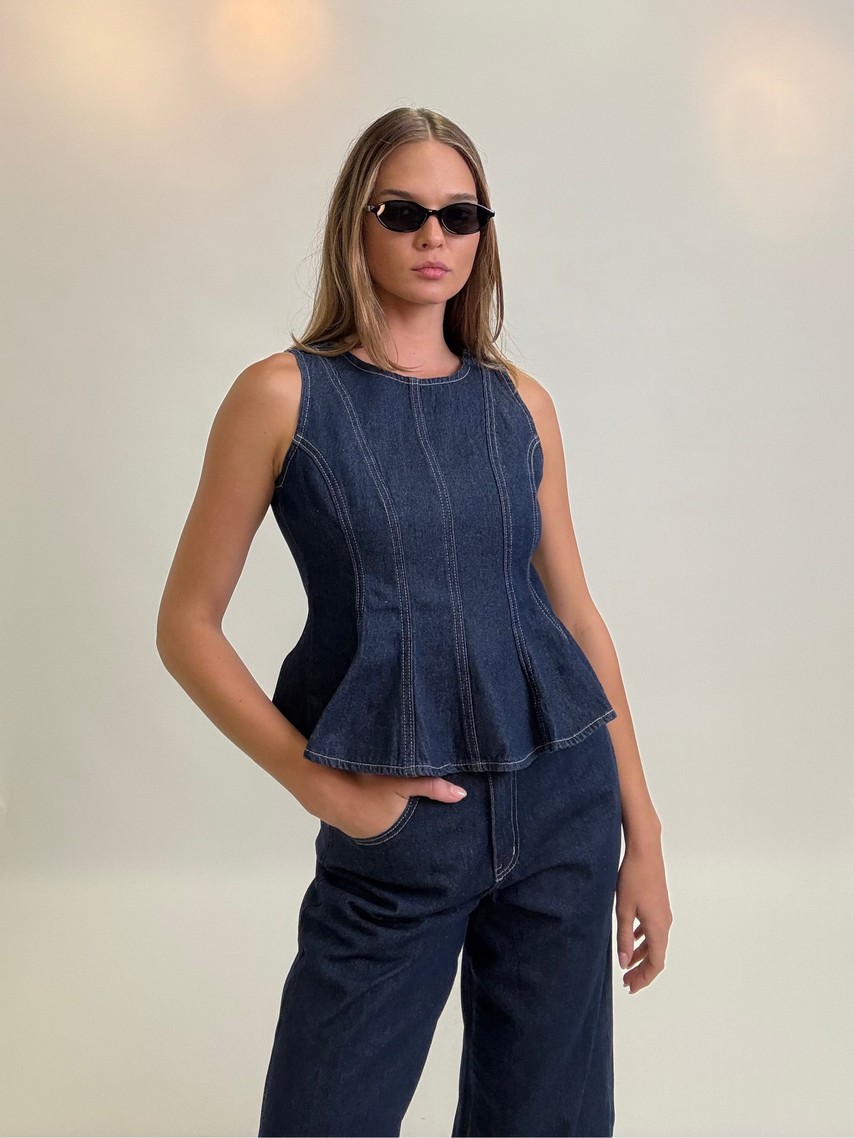 Woman wearing a denim peplum top and pants in a studio setting