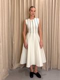 Woman wearing a white dress with black patterns against beige curtains